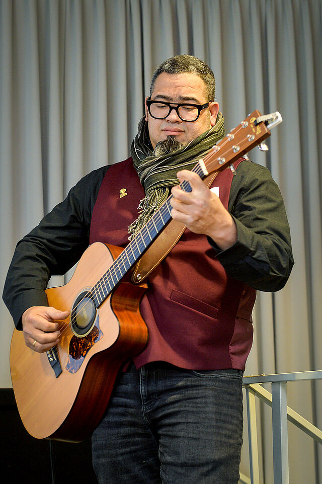 Christian Pichardo steht mit einer Gitarre auf der Bühne und singt. Er trug den musikalischen Rahmen zu der Veranstaltung bei