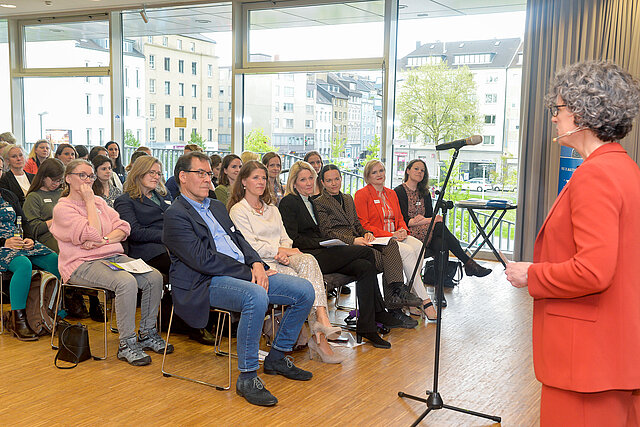 Die Moderatorin Susanne Küsters spricht vor der Bühne zum Publikum.